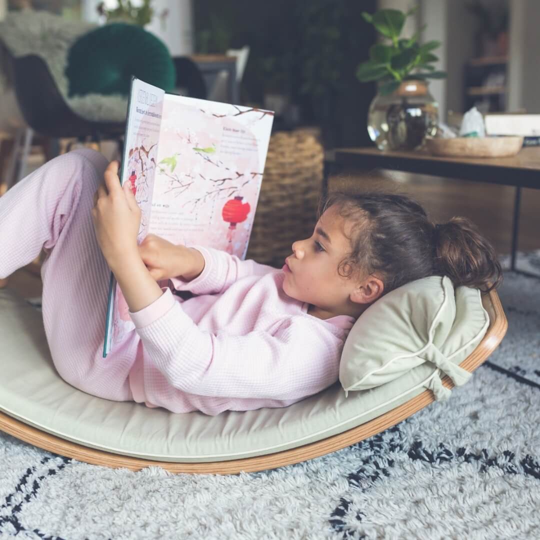 Child relaxing on a Wobbel Board with cosy fabric Wobbel Deck and Pillow - an inviting playroom reading nook, at Wooden Playroom in Australia