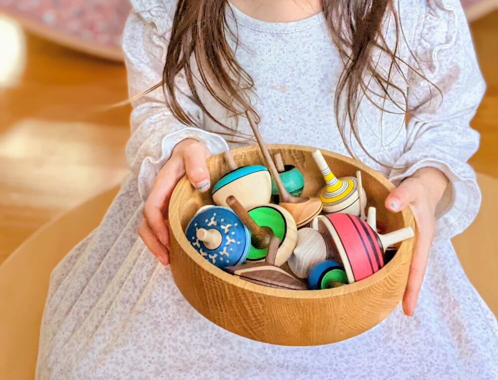 Girl holding collection of Mader wooden spinning tops, distributed in Australia by Wooden Playroom