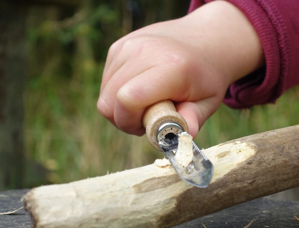 Child whittling a stick outdoors with a Kids at Work whittling peeler knife at Wooden Playroom in Australia