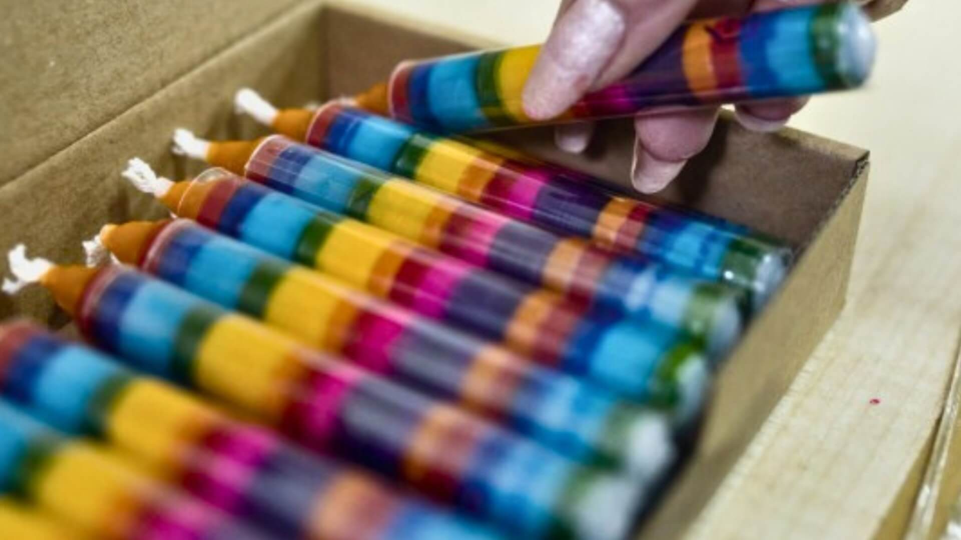 Colorrful Ahrens candles in a box with a hand holding one above.