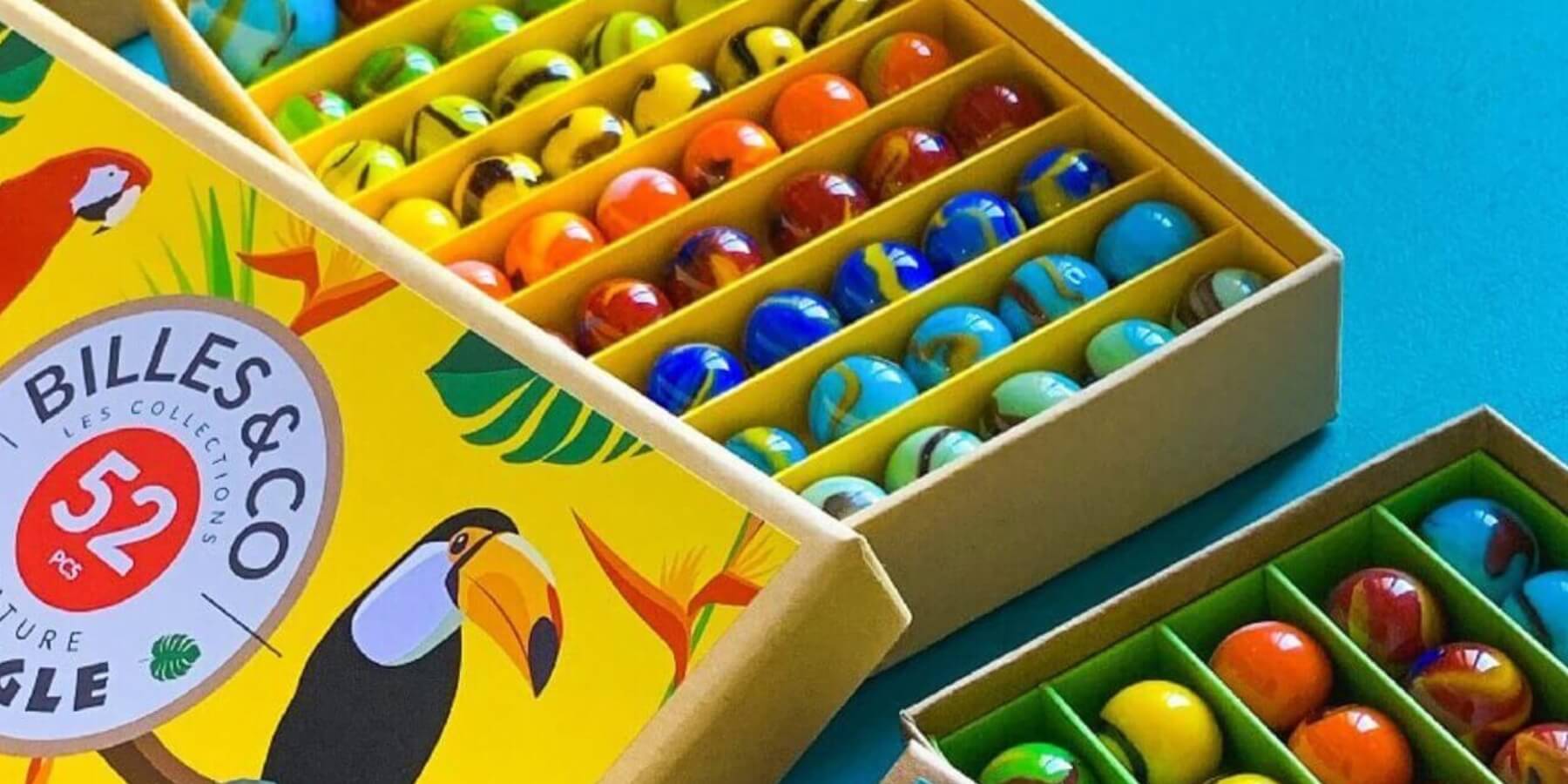 Colorful marbles in an open box with 'Billes & Co' branding on a blue background