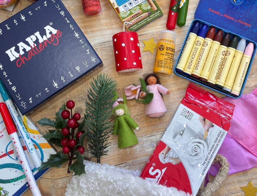 Assorted art supplies for Christmas Stockings, including Stockmar crayons, Giotto markers, and Kapla building blocks on a wooden surface. 