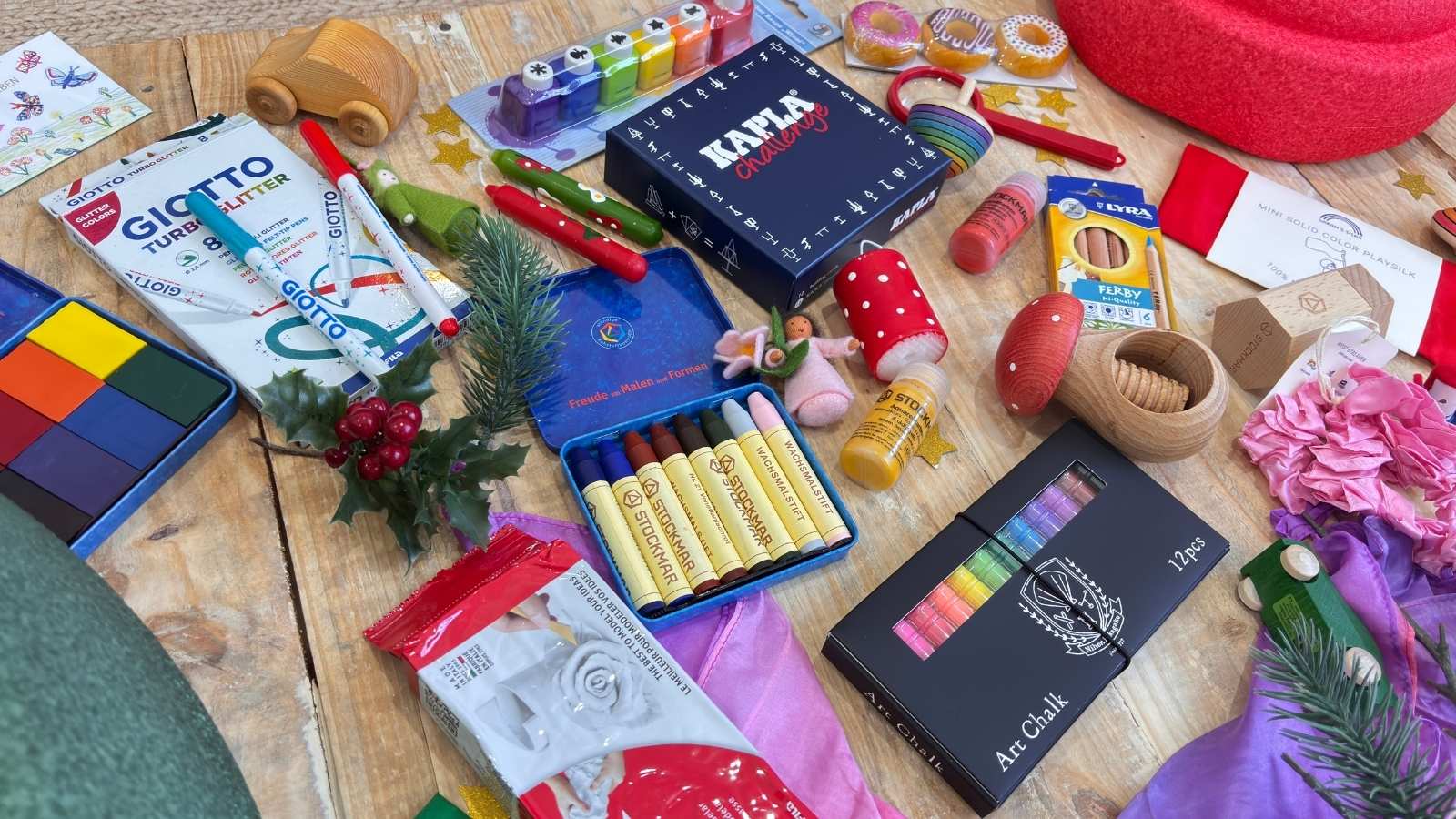 A styled flat-lay of various colourful children's art and craft supplies and toys on a wooden surface, with a Christmas theme