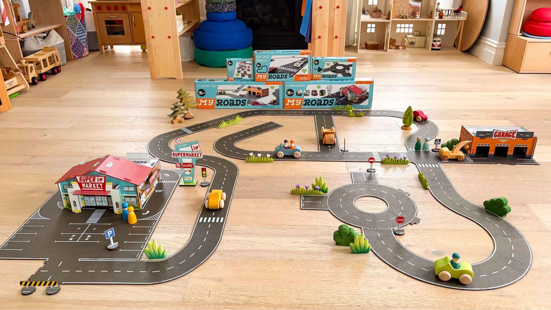 Toy road set from Magellan My Roads with buildings, cars, and traffic lights on a wooden floor