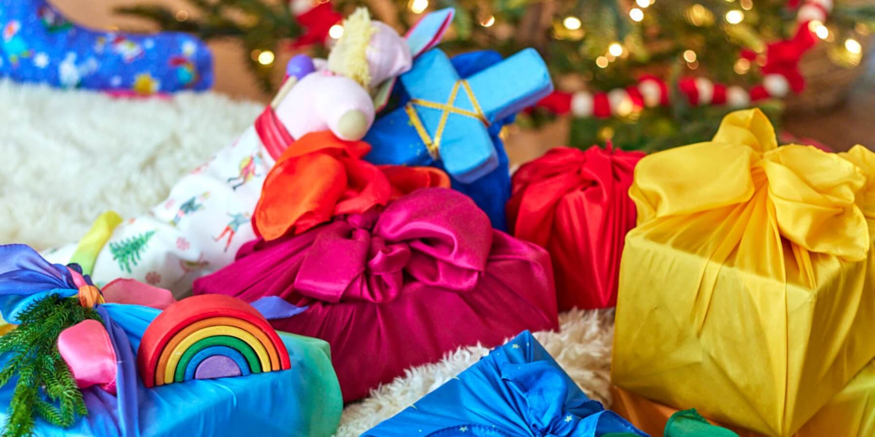 Colourful gifts wrapped in Sarah's Silks Playsilks, Christmas tree in the background