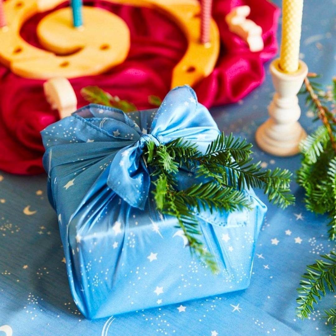 Gift wrapped in a Sarah's Silks play silk with a candle and Christmas decorations in the background