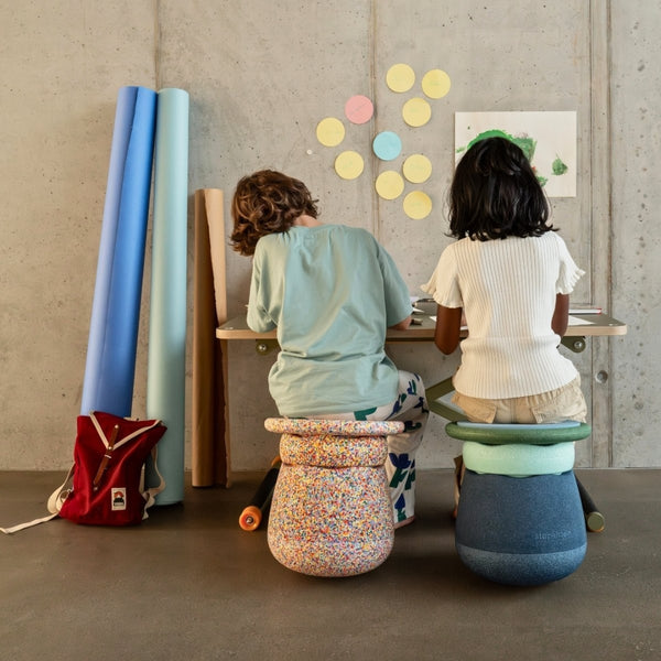 Two children sitting on colourful Stapelstein Dynamic stools at a desk with art supplies.