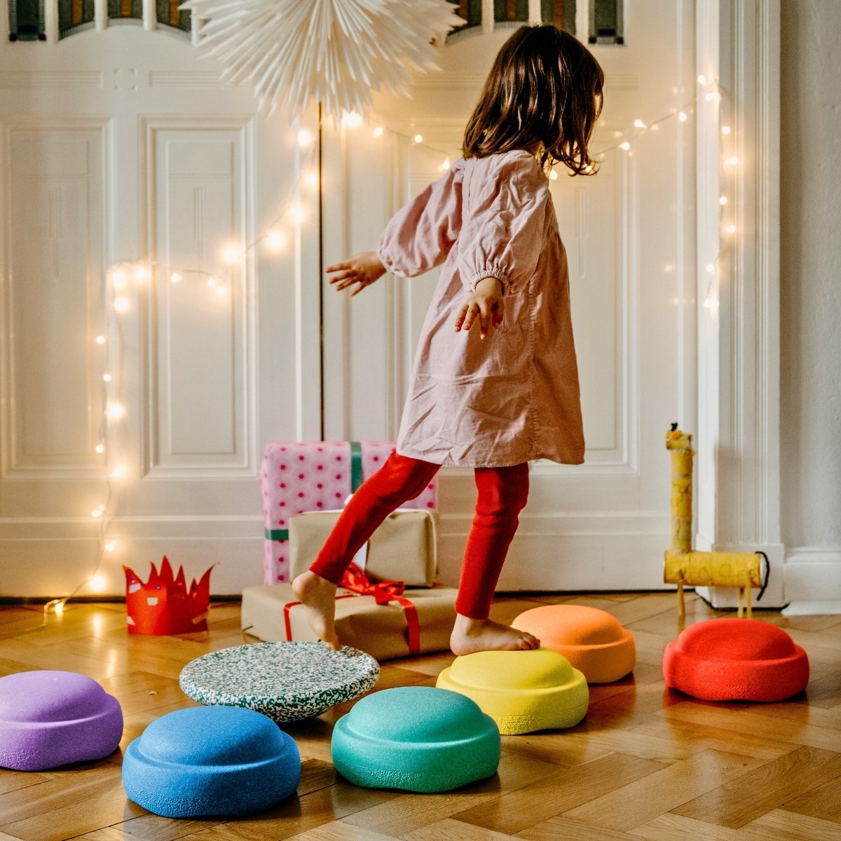 Child playing with colorful stools in a room decorated with string lights